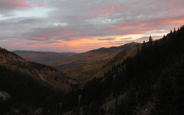 The sky appears in soft shades of pink, purple and orange as the sun sets or rises on a mountainous landscape